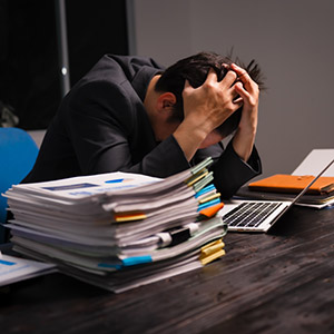 Distressed person at desk with many papers, laptop; symbolizing financial stress/bankruptcy.